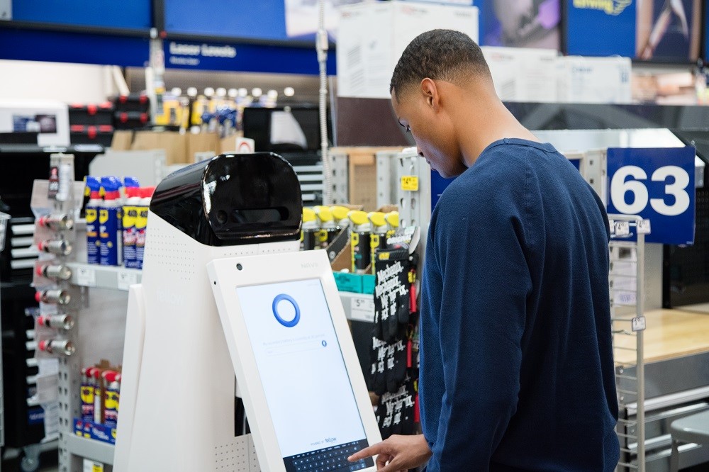 A man standing at a self-checkout kiosk in a store, looking at the screen.