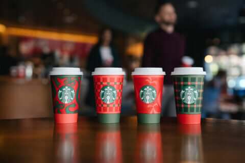 Four coffee cups on table, each with a holiday-themed lid.