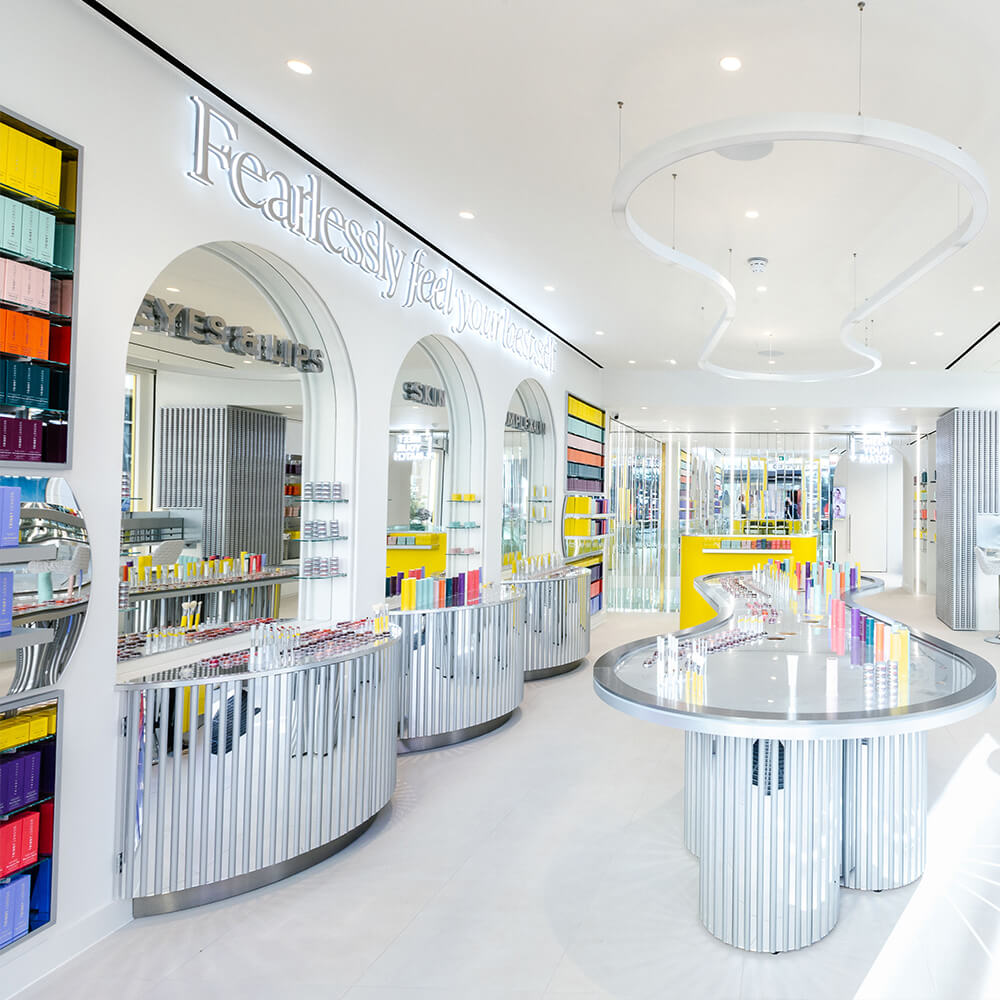 An interior view of a store, featuring a large display of cosmetics products, including makeup brushes and lipsticks, arranged on shelves and…