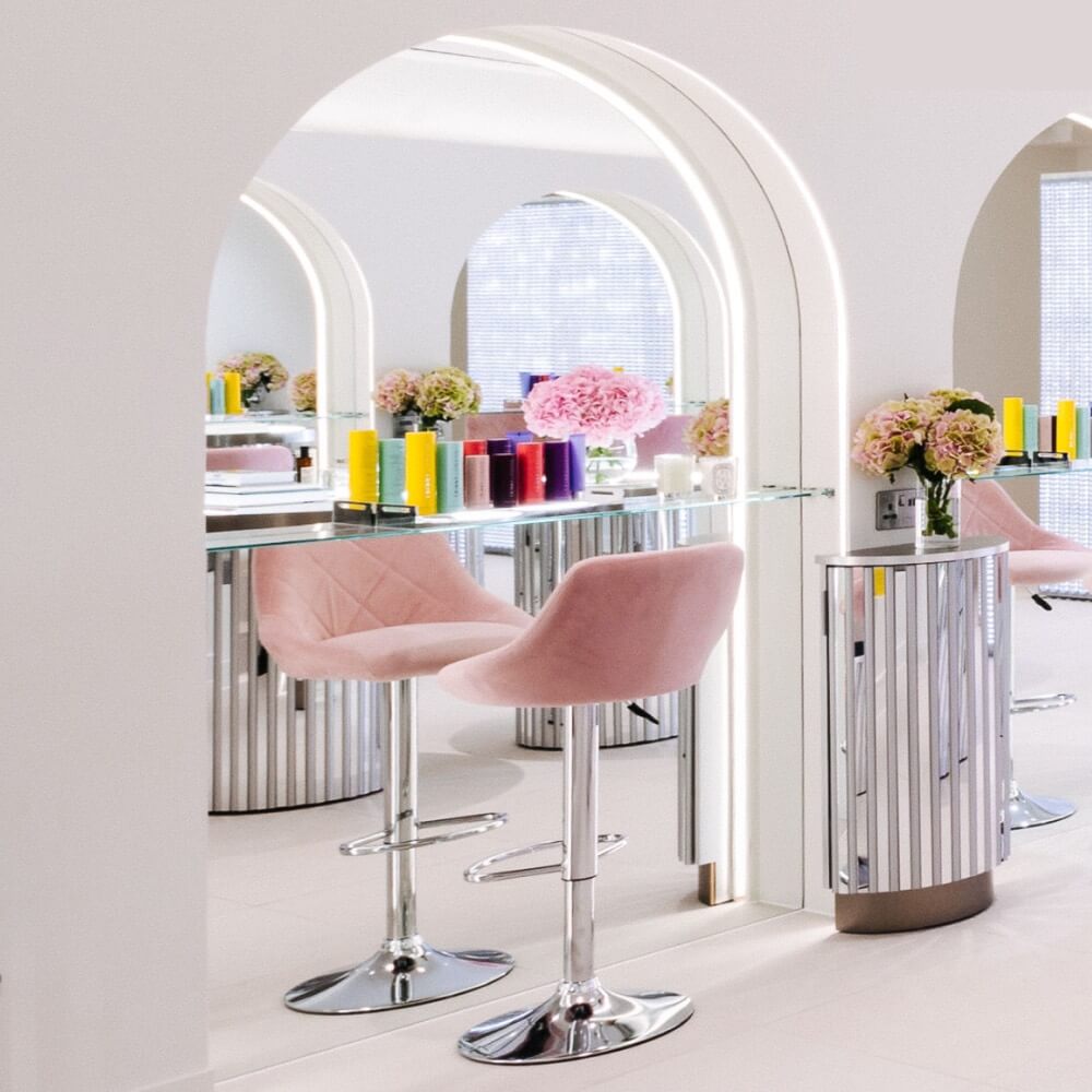 A modern salon with pink chairs, white counters, and a large mirror.