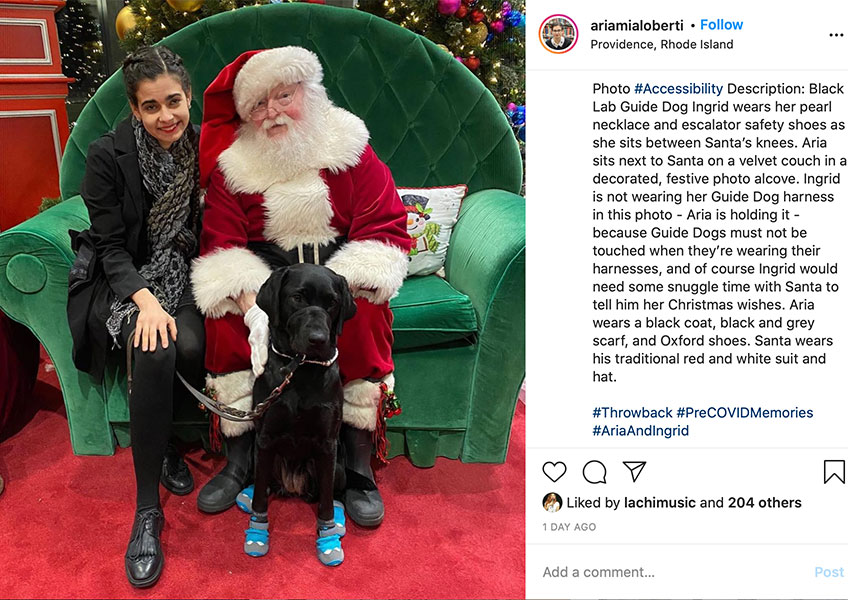 A woman posing with a dog dressed as santa claus, standing in front of a Christmas tree.