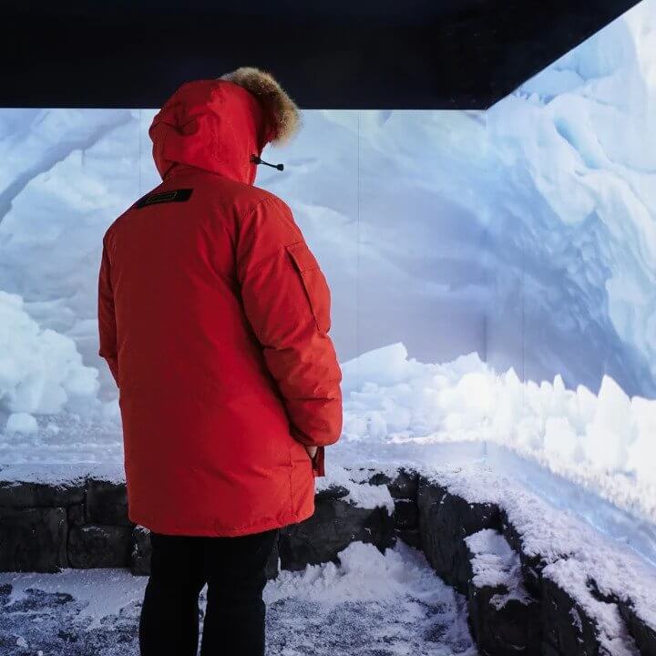 Person standing in front of an ice wall, wearing a red jacket and hat, looking at the camera.
