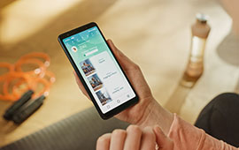 A person holding a smartphone displaying a social media app, with the phone screen showing a feed of posts.