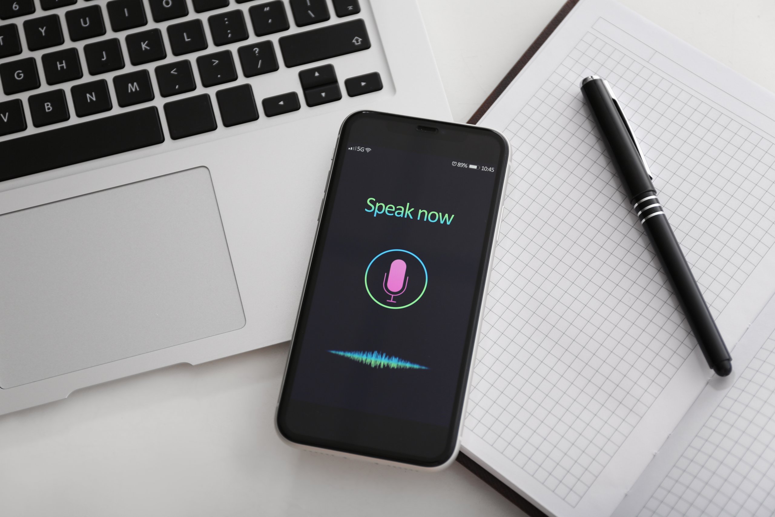 A smartphone displaying a voice assistant app on the screen, placed next to a notebook and pen on a desk.
