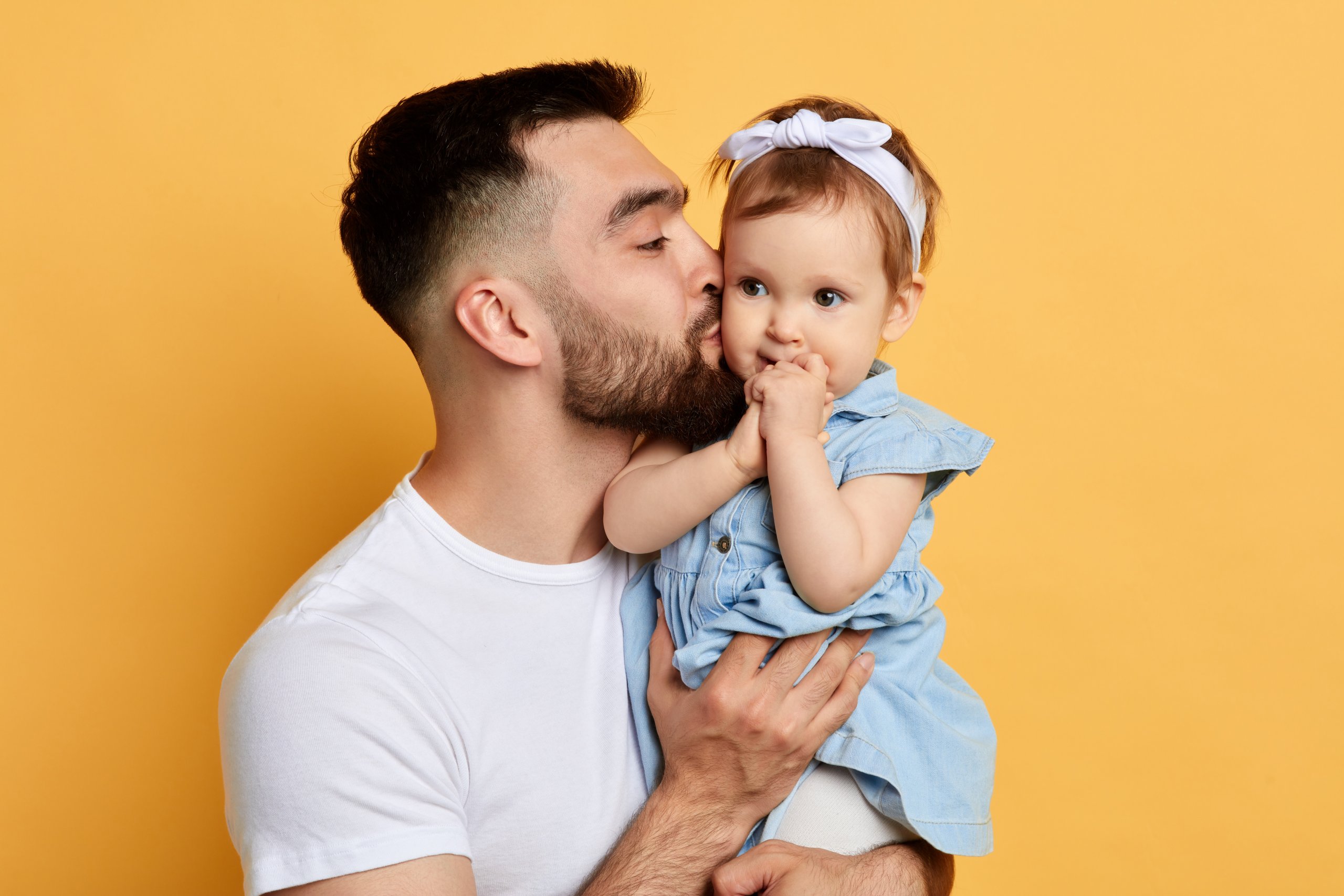 Man holding baby close to his face, both smiling, against yellow background.