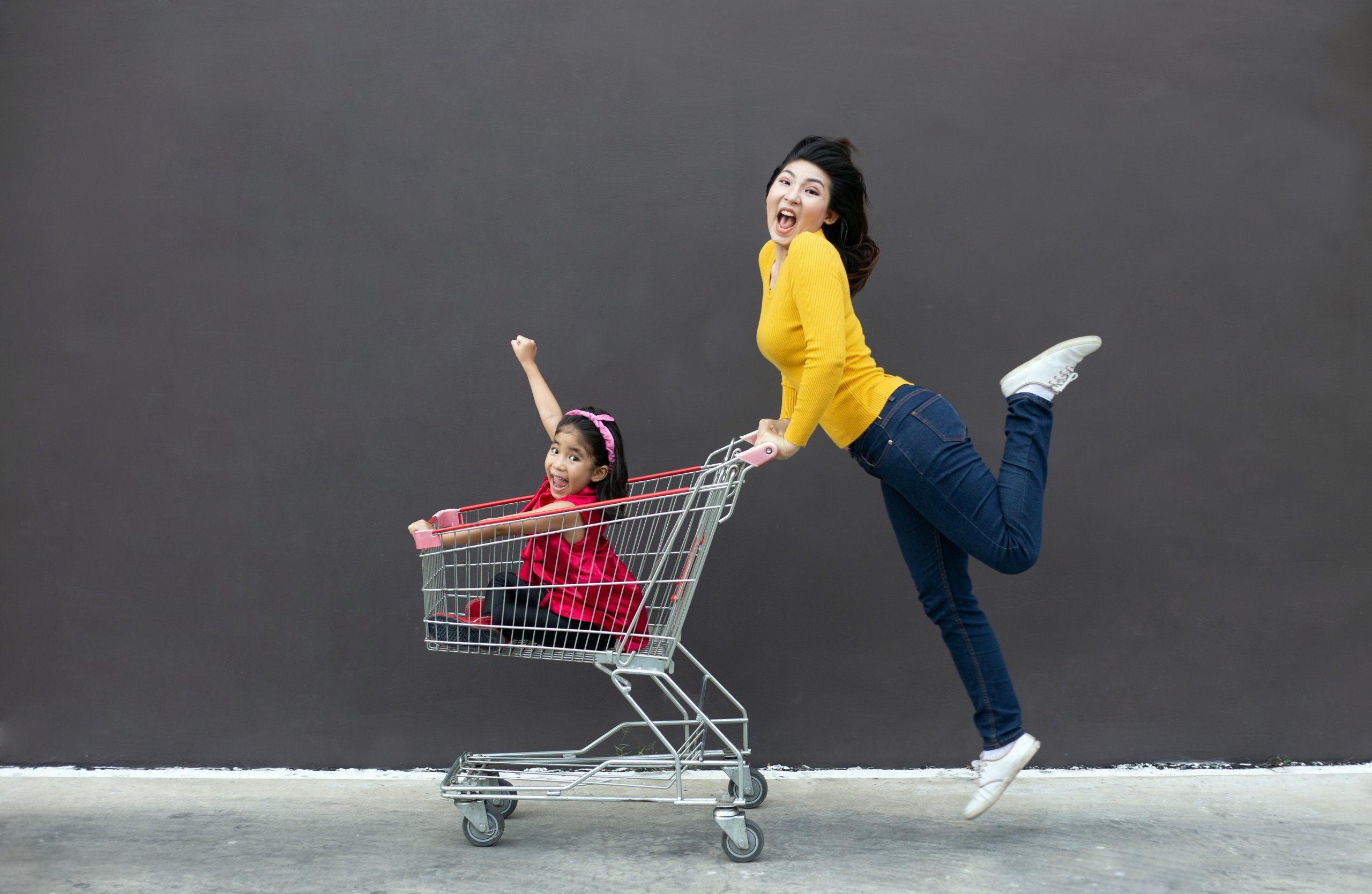 A woman pushing a child in a shopping cart, both are in motion