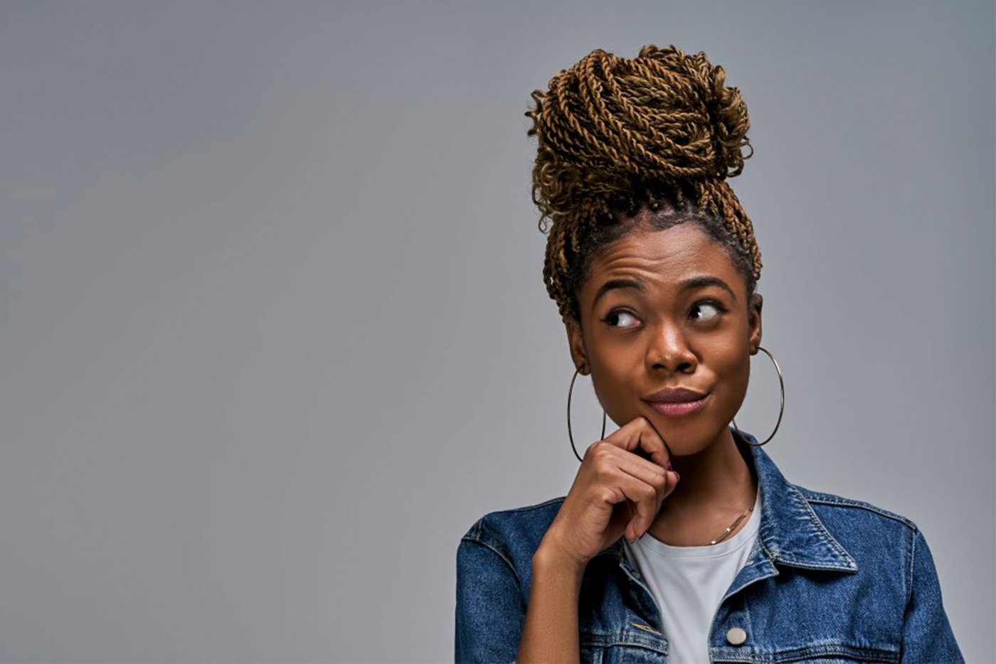 Woman with braided hair, wearing a denim jacket, posing with hand on chin.