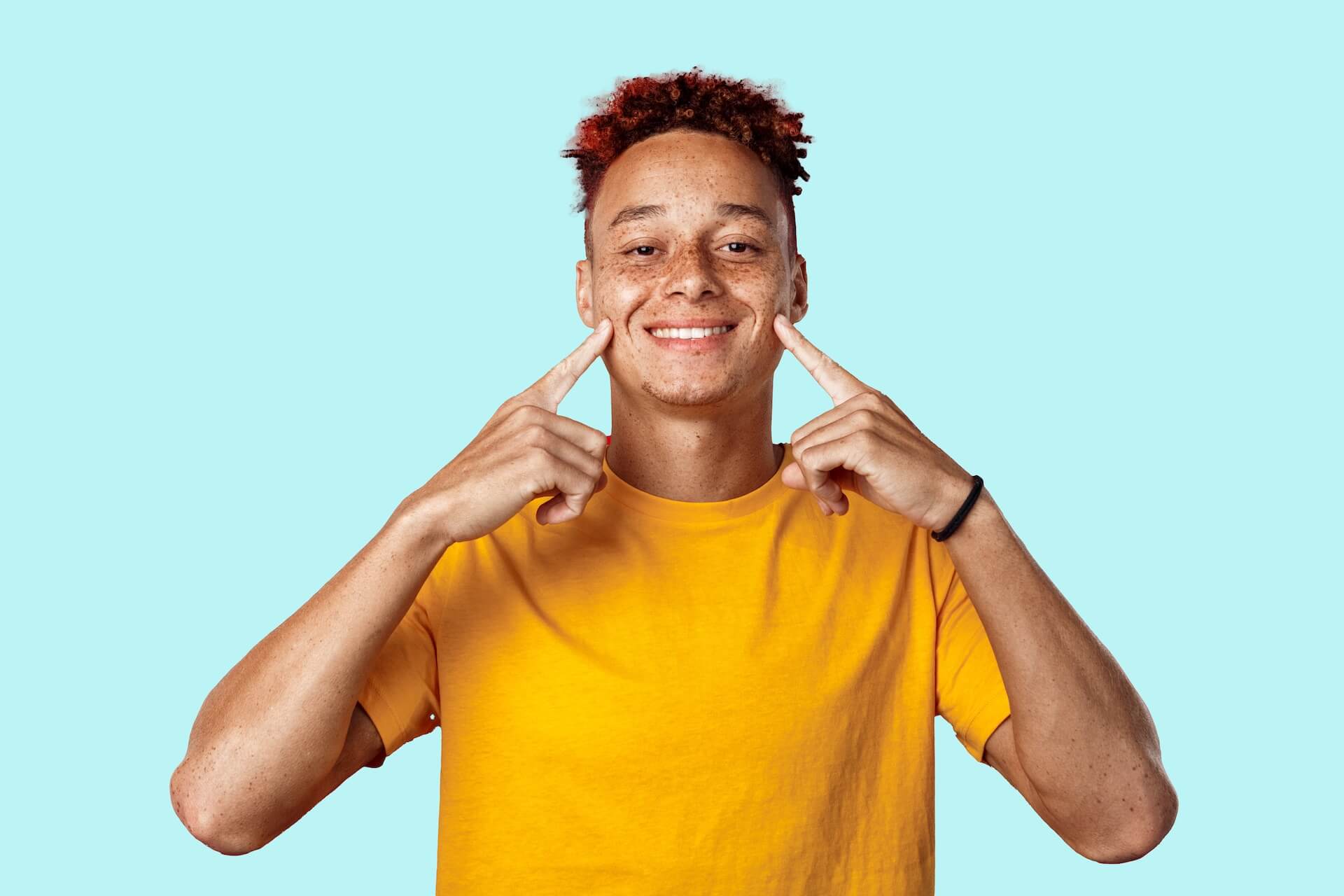 A young man with red hair, wearing a yellow t-shirt, making a funny face with his fingers.