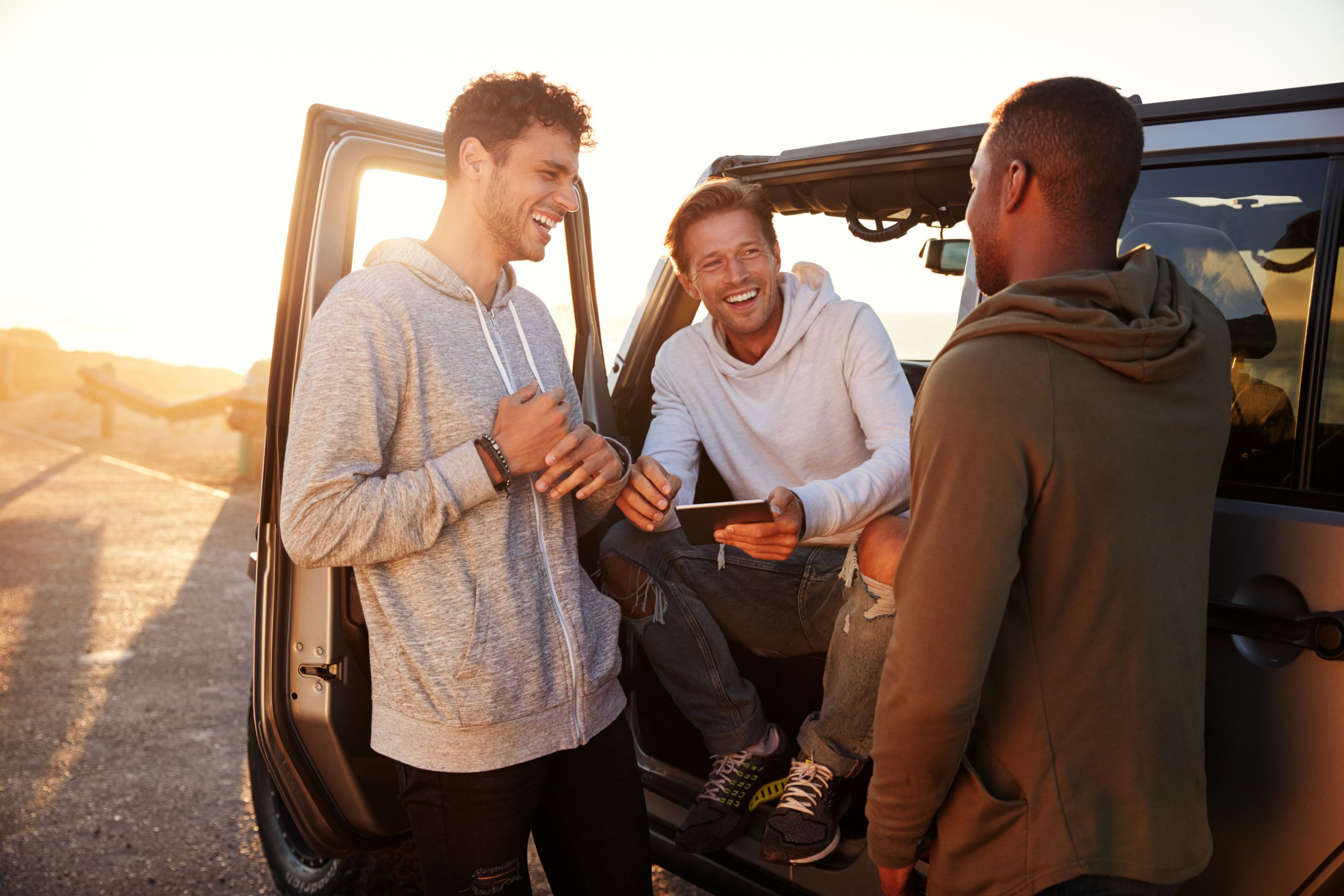 Two men standing in the back of a jeep, smiling and talking to each other.