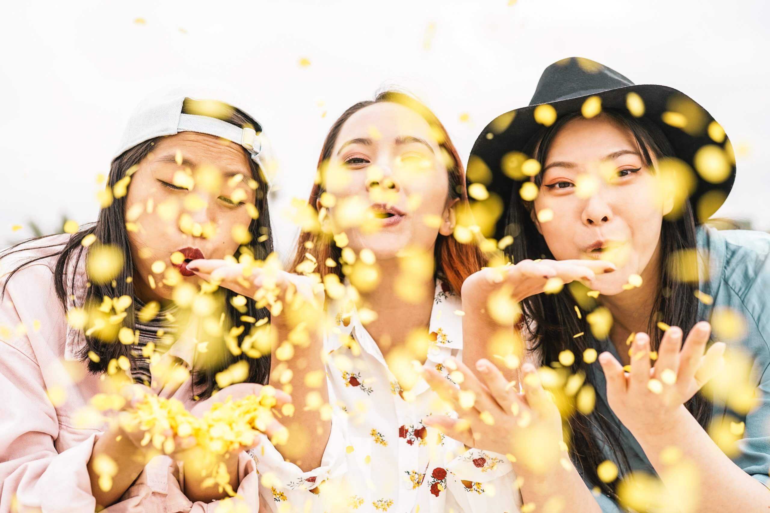 Three people, two women and one man, posing together in front of confetti.
