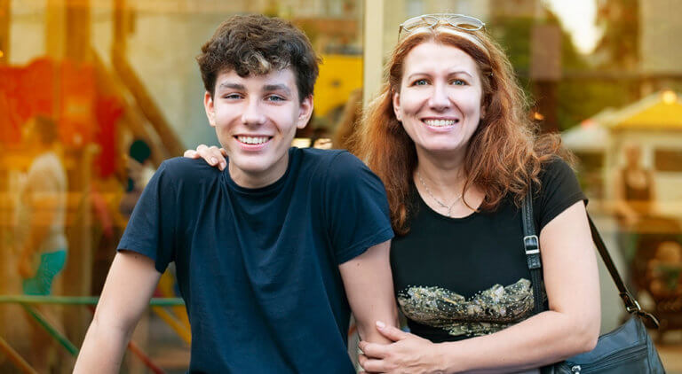 A young man and an older woman posing together in front of a storefront.