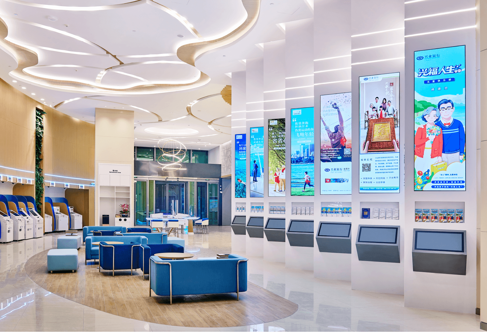 An interior view of a modern lobby, featuring a large digital display screen, seating area, and information boards.