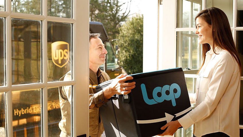 A woman handing a box to a man, who is holding it open. They are standing in front of a window.