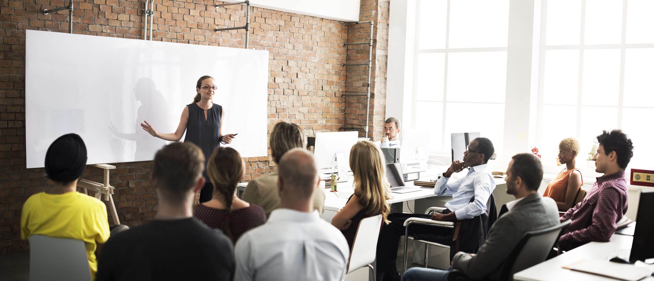 A woman standing at the front of a classroom, teaching a group of people.