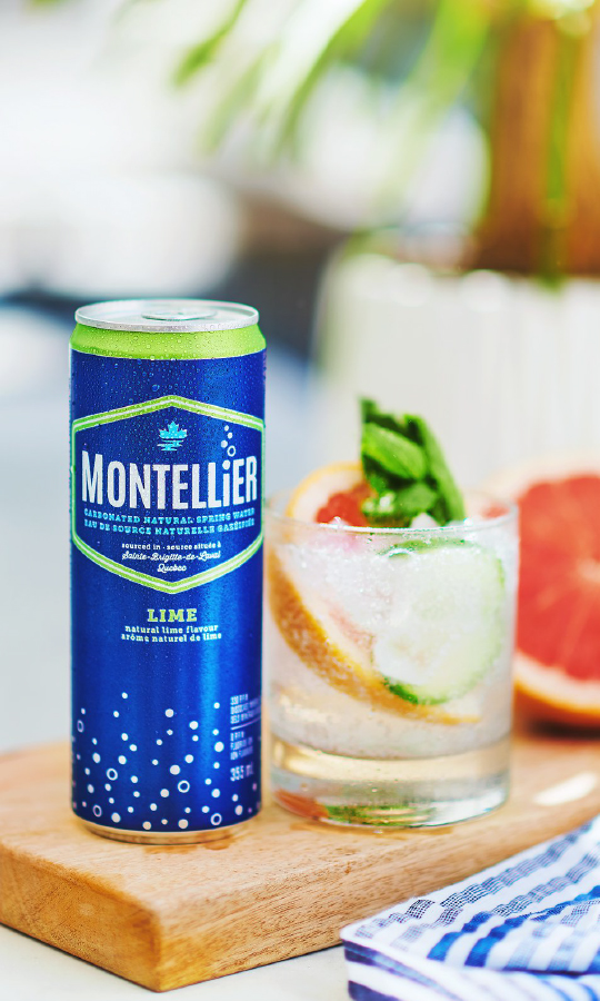 A can of Montezuma lime soda on a wooden table next to a glass of water with lemon slices.
