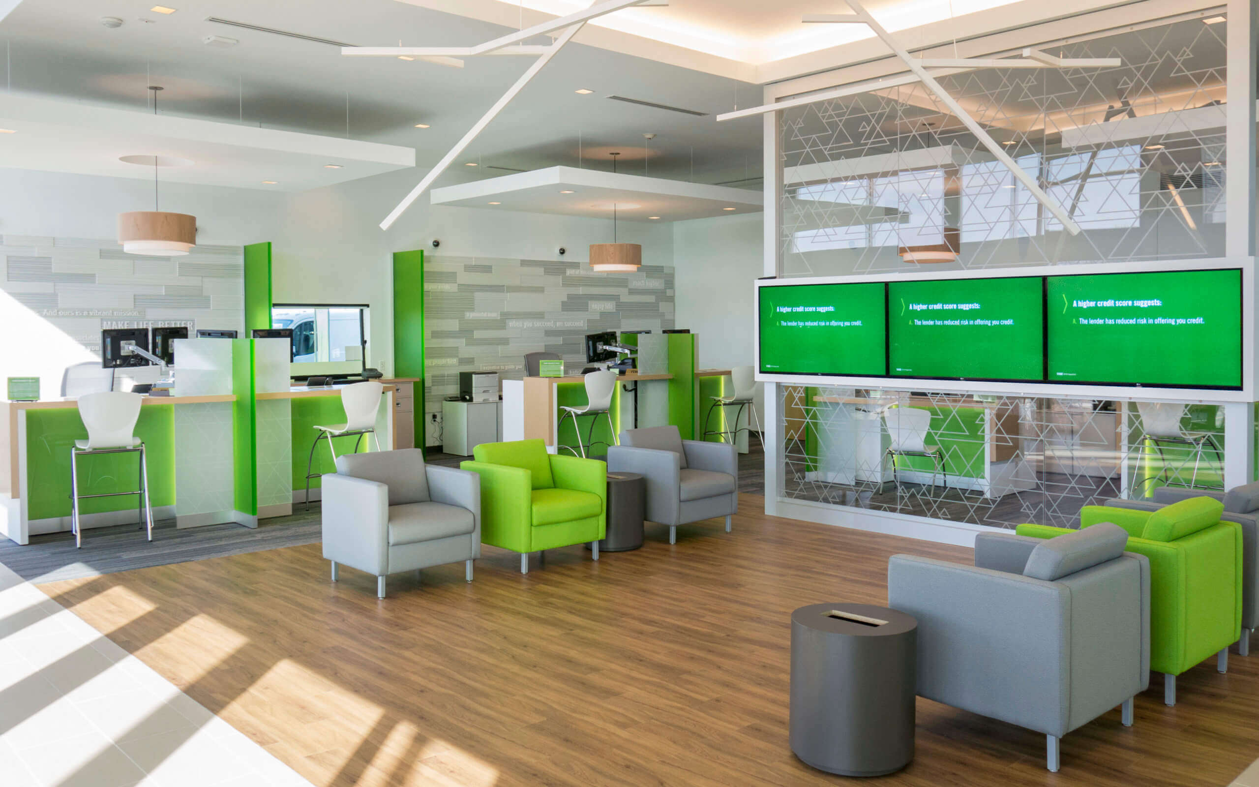 A modern waiting room with green seating, white walls, and a large screen displaying information.