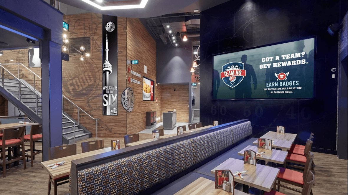 A modern sports bar interior with seating, televisions, and a large screen displaying an advertisement.