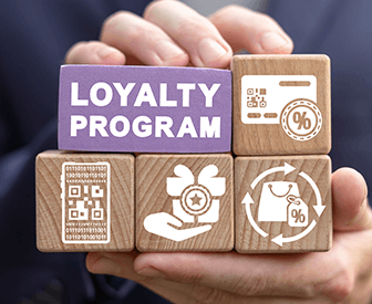A hand holding a wooden block with the words "loyalty program" on it, surrounded by various icons related to loyalty programs.