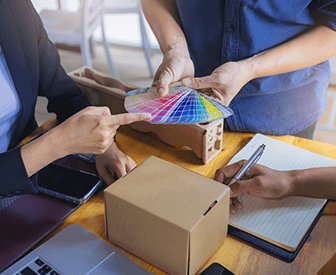 A group of people gathered around a table, examining a colorful object in a box, possibly a paint sample or a piece of art.