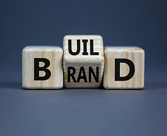 Three wooden blocks with the letters "UIL" on top, "BRAND" in the middle, and "D" at the bottom, arranged to spell out "UI L B D.