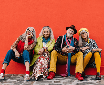 A group of four people posing together, all wearing colorful clothing and accessories.
