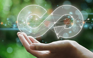 A hand holding a glowing, interconnected symbol that resembles a recycling sign, set against a blurred background with bokeh lights and a hint of…