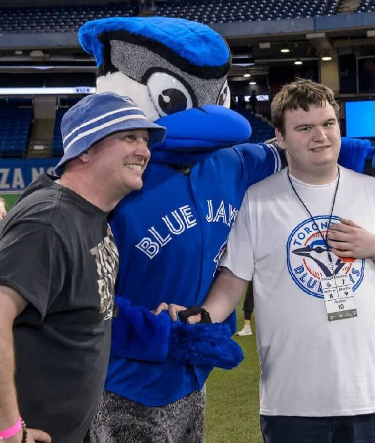 Two men posing with a mascot in front of a stadium.