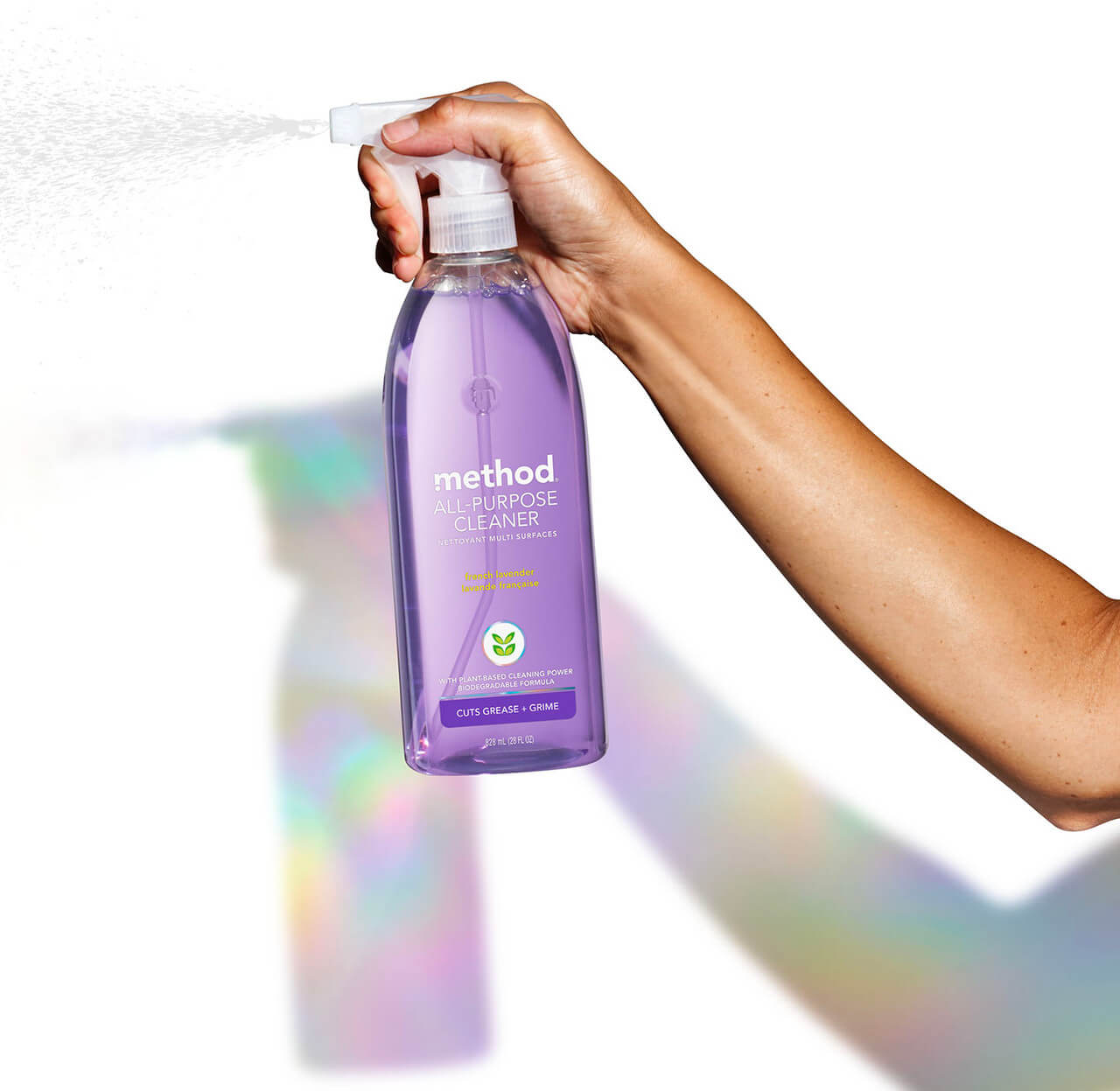 A hand holding a bottle of Method soap, spraying it towards the camera.