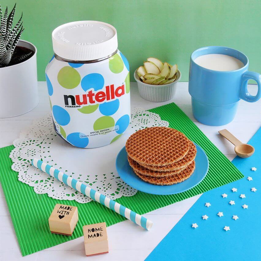 A table setting with a jar of Nutella, waffle cookies, a cup of coffee, and a spoon.