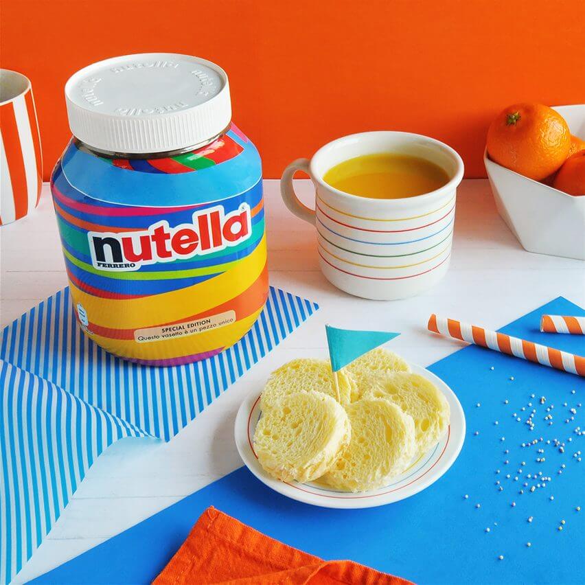 A jar of Nutella on table, next to a plate of cookies, a cup of tea, and a bowl of fruit.