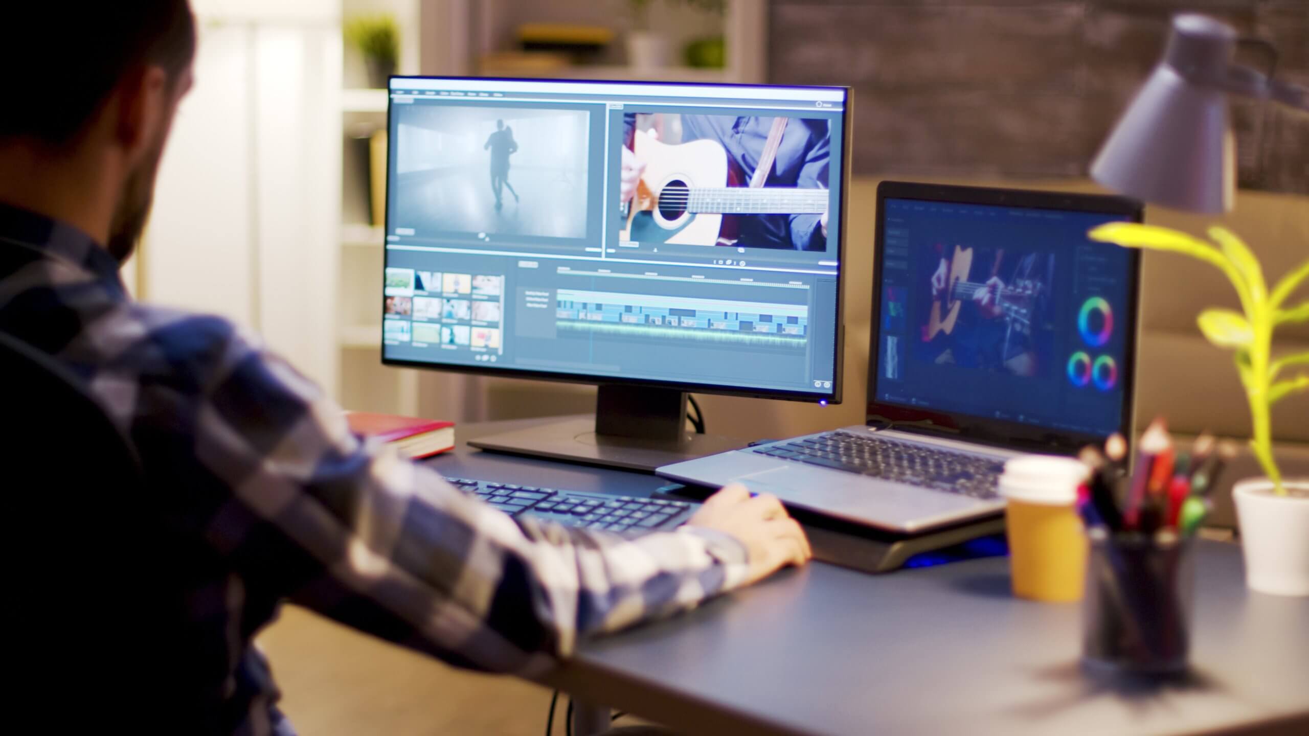 A man sitting at a desk working on a computer in front of two monitors displaying video footage.