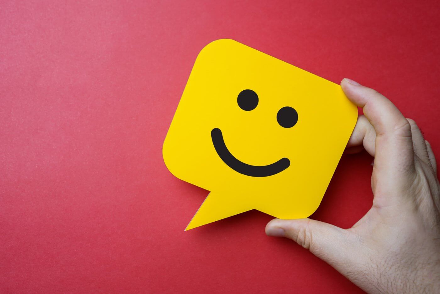 A hand holding up a yellow smiley face sticker on a red surface.