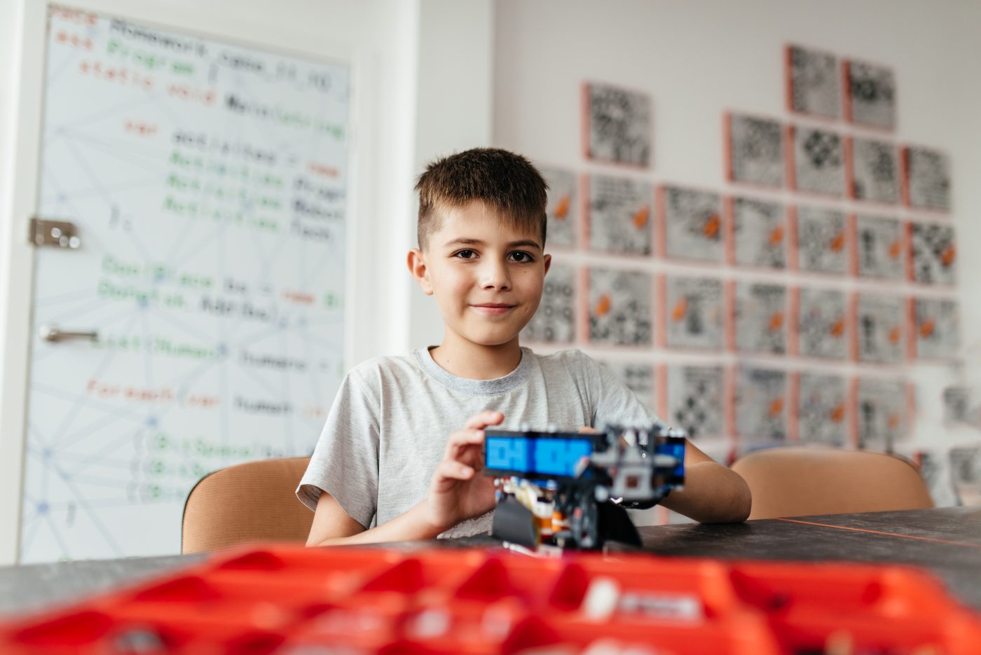 A young boy sitting at a table with a red remote control car in front of him.