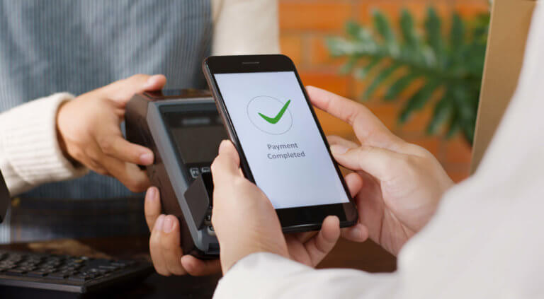 A person holding a smartphone, showing a green checkmark on the screen, indicating approval or confirmation.