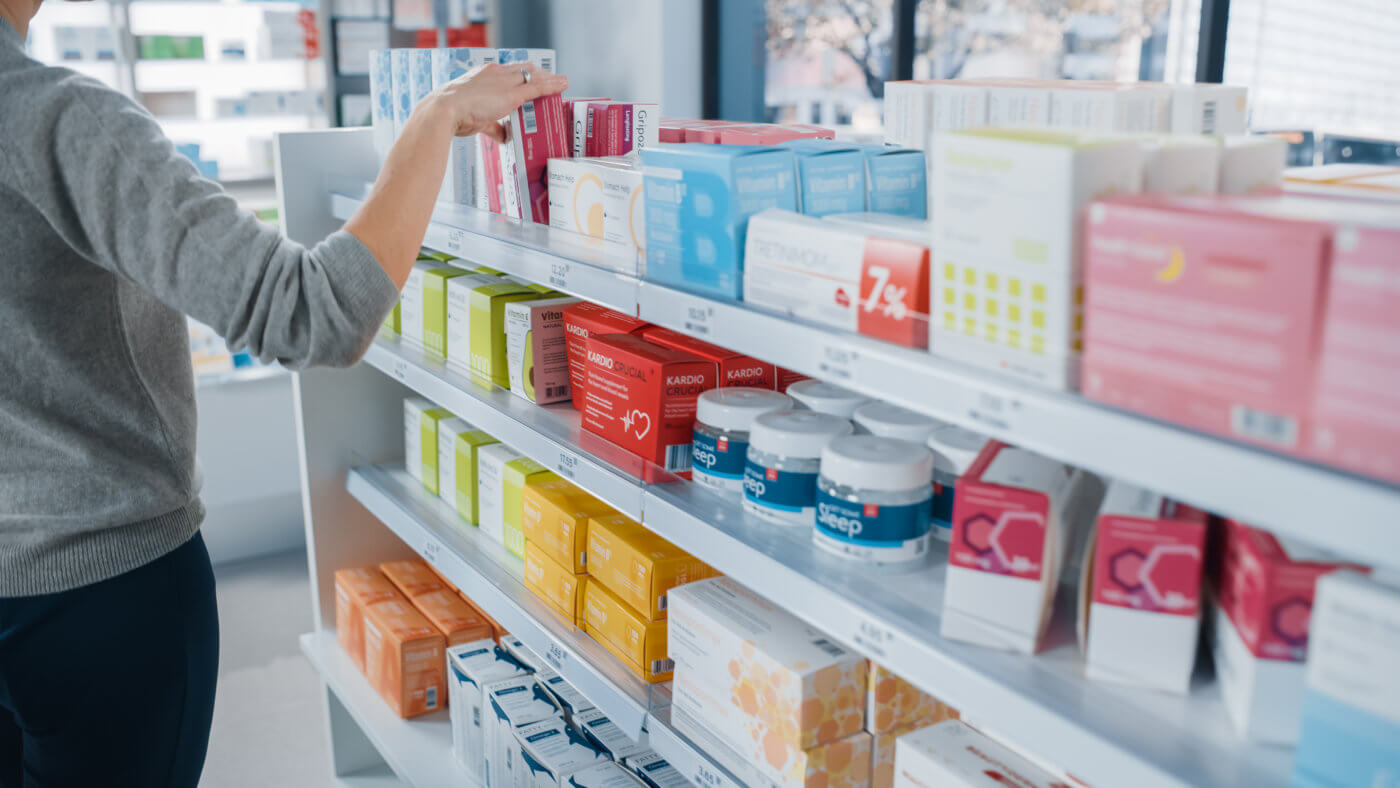 A person standing next to a shelf stocked with various products, likely in a store or pharmacy.