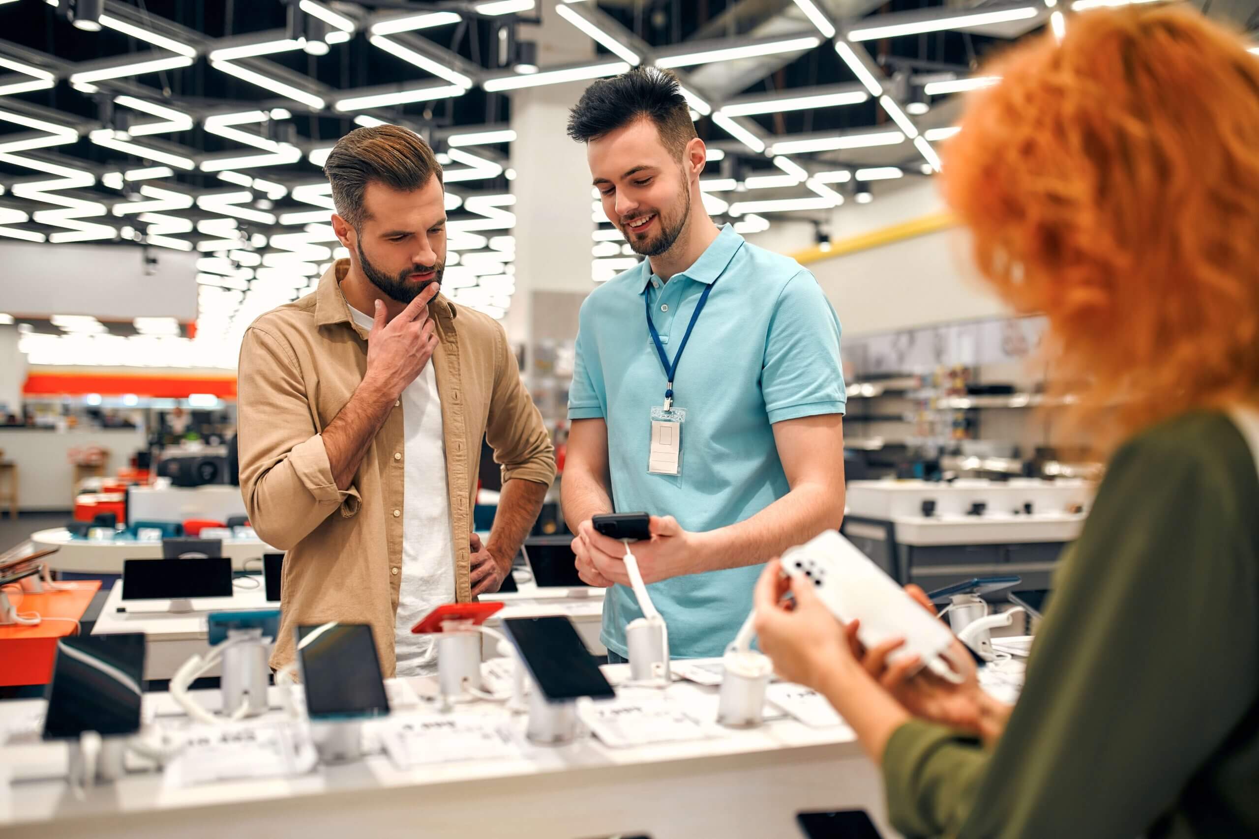 Two men standing in a store, smiling at the camera. A woman behind them looking at items on display.