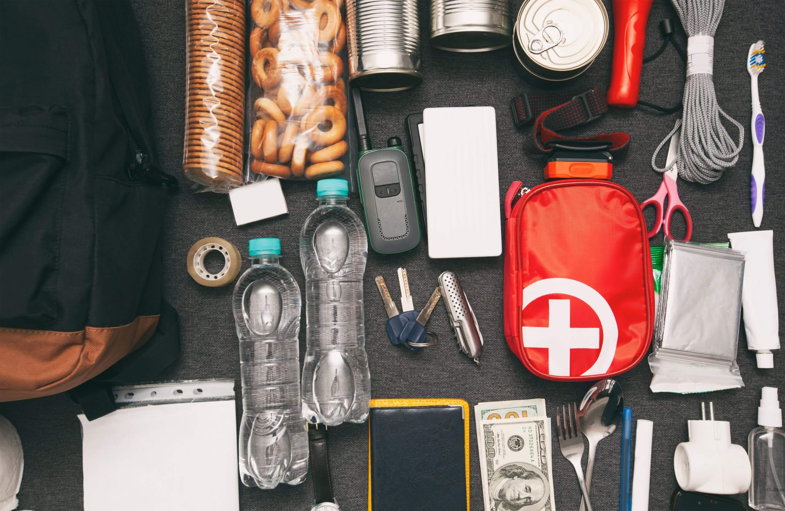 A collection of items on a table, including a first aid kit, snacks, tools, and personal belongings.