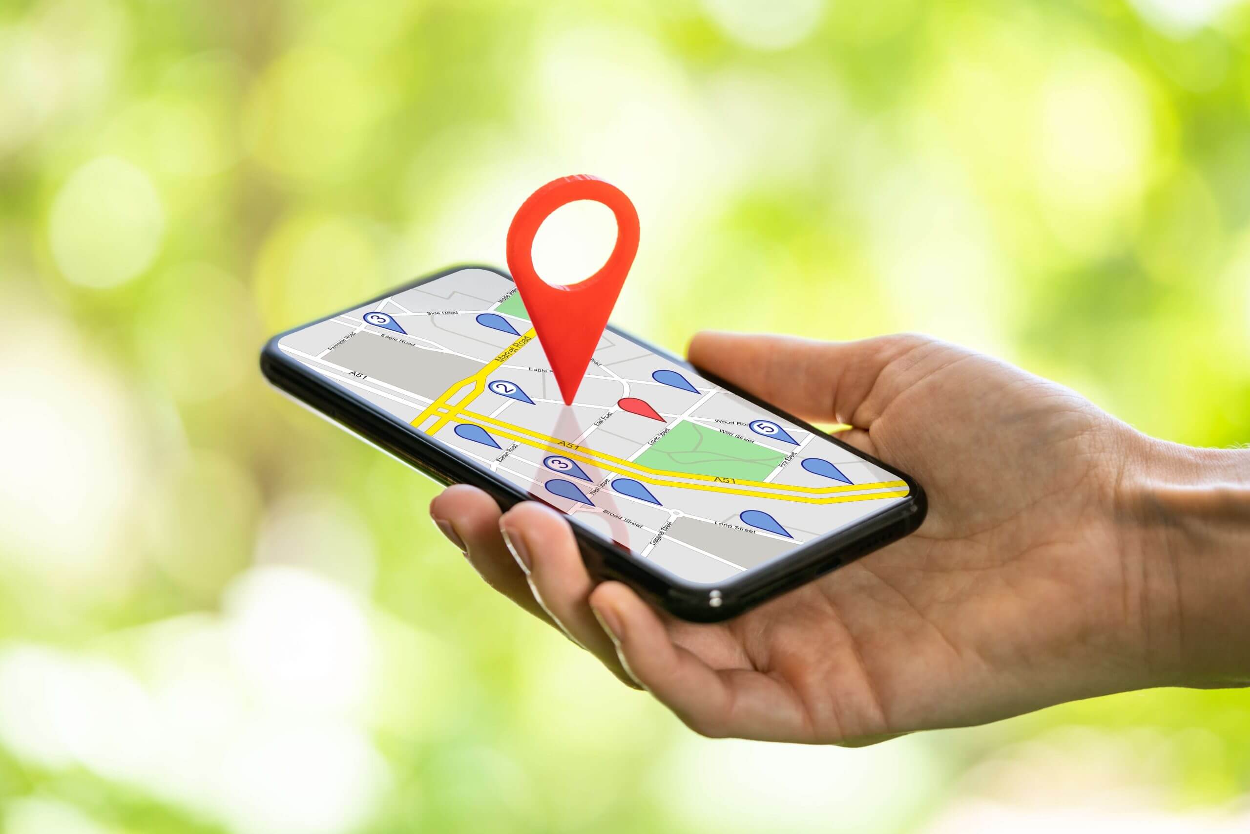 A hand holding a smartphone displaying a map with a red pin on it, suggesting location tracking or navigation.