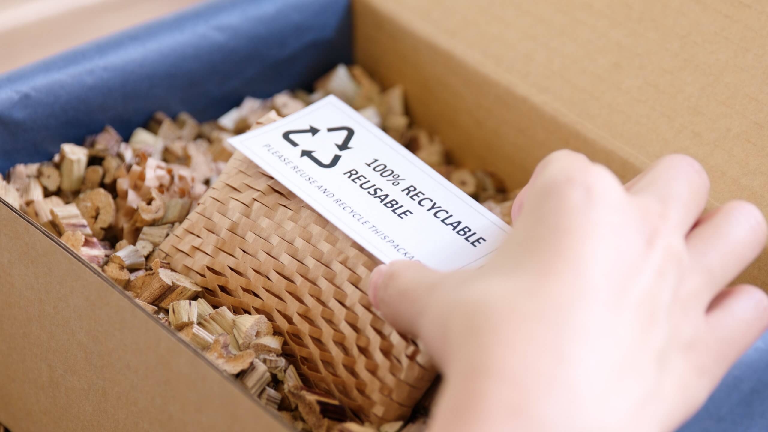 A hand reaching into a box filled with shredded paper, revealing a small cardboard sign.