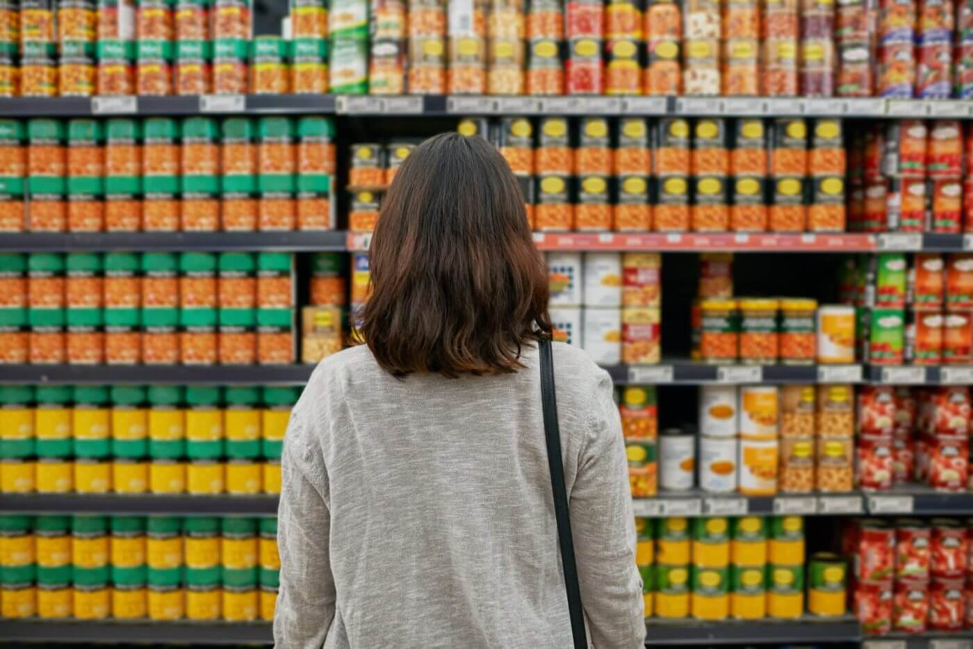 Woman standing in front of grocery store shelves filled with canned goods.