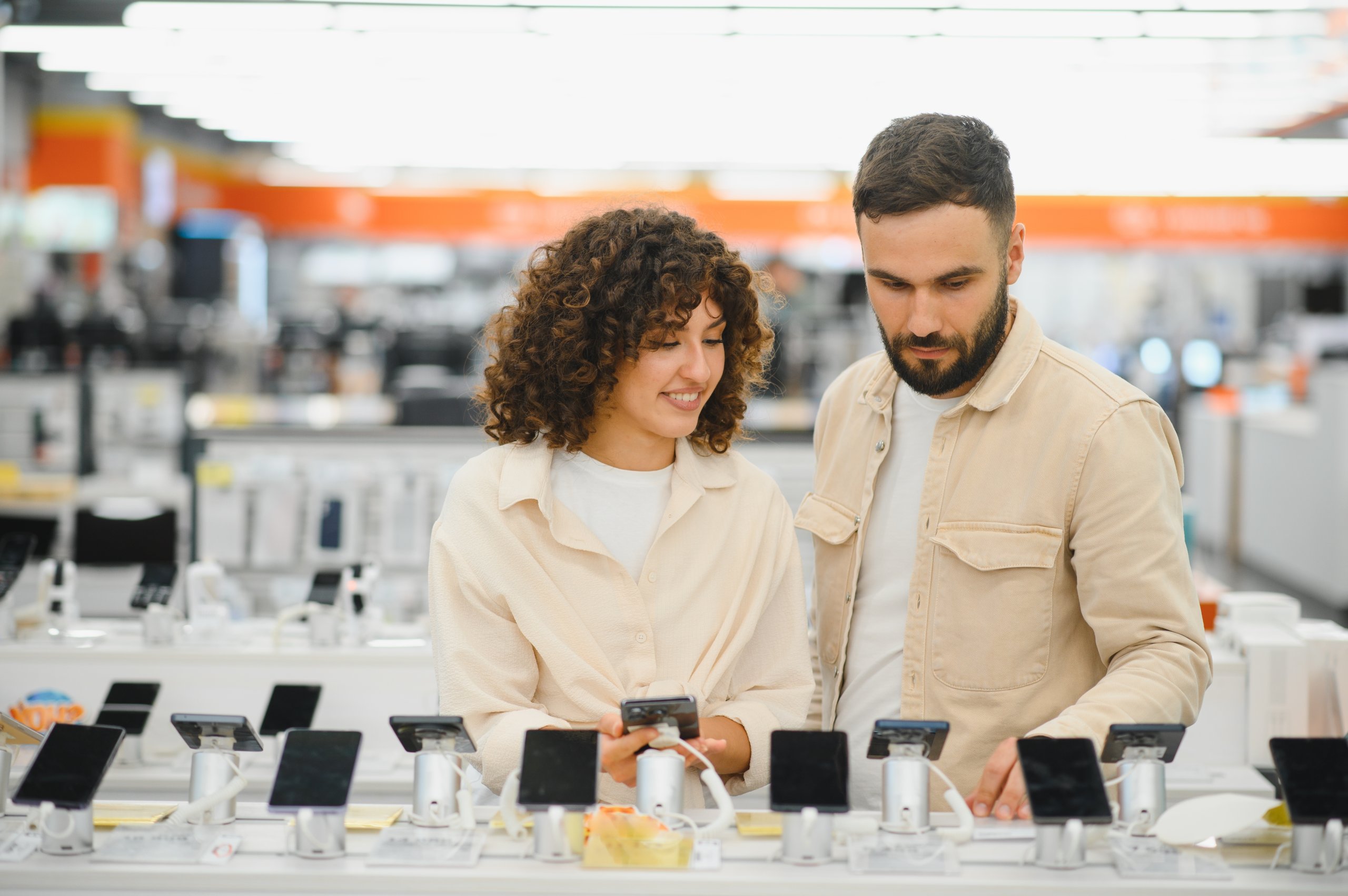 Two people standing in an electronics store, looking at a display of cell phones.