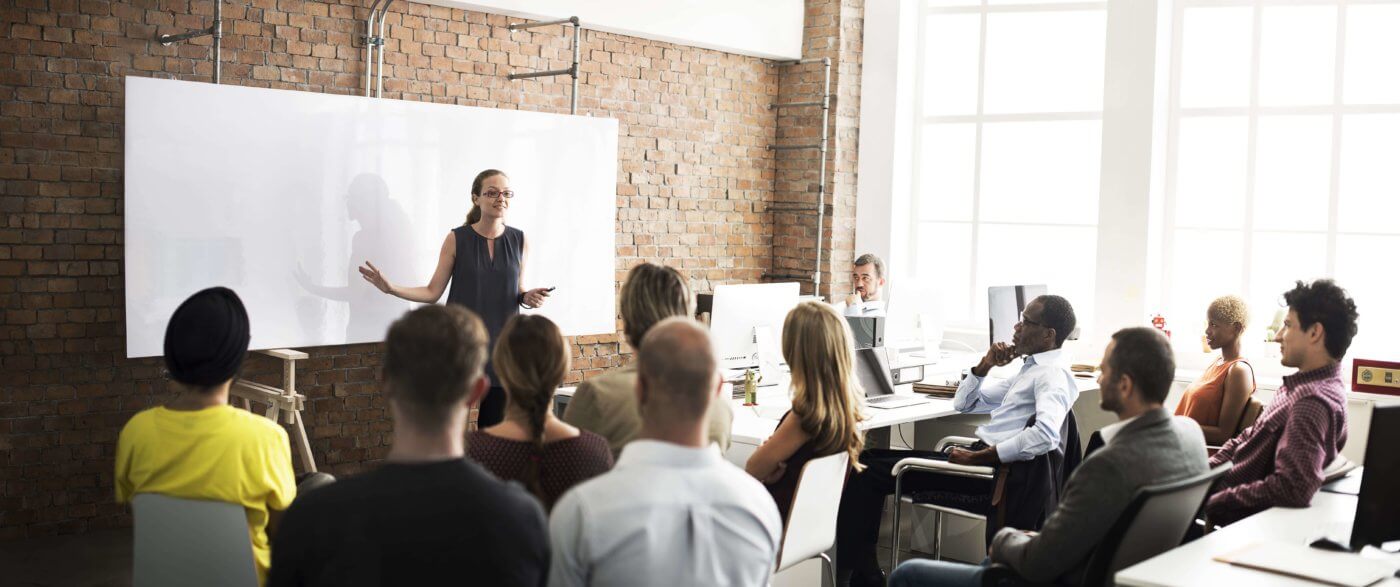 A group of people gathered around a whiteboard in a classroom setting, listening to a presentation.