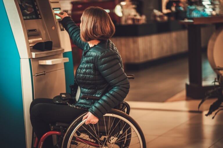 Woman sitting on wheelchair at an atm machine, looking at the camera.